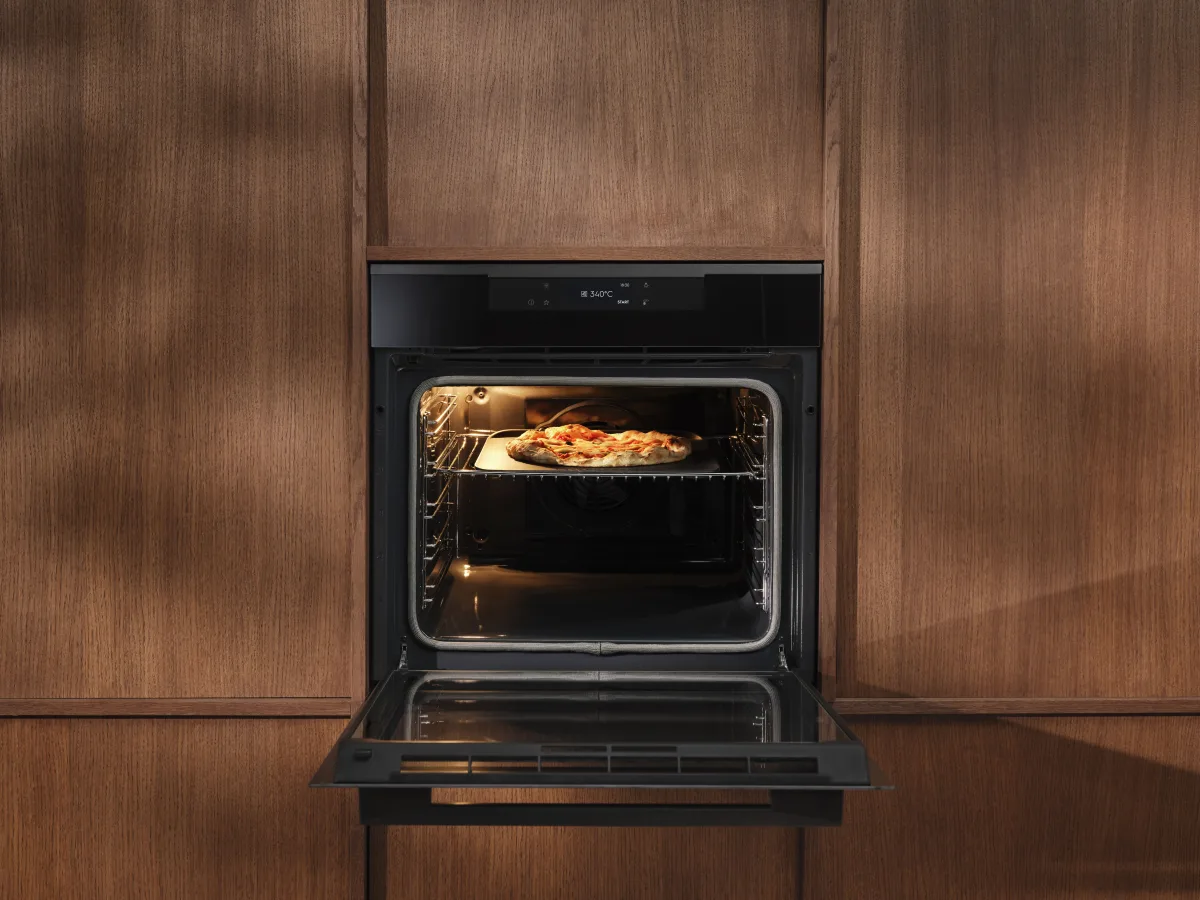 Forno Electrolux PizzaExpert Serie 700 aperto con una pizza sulla griglia, incassato in una parete in legno