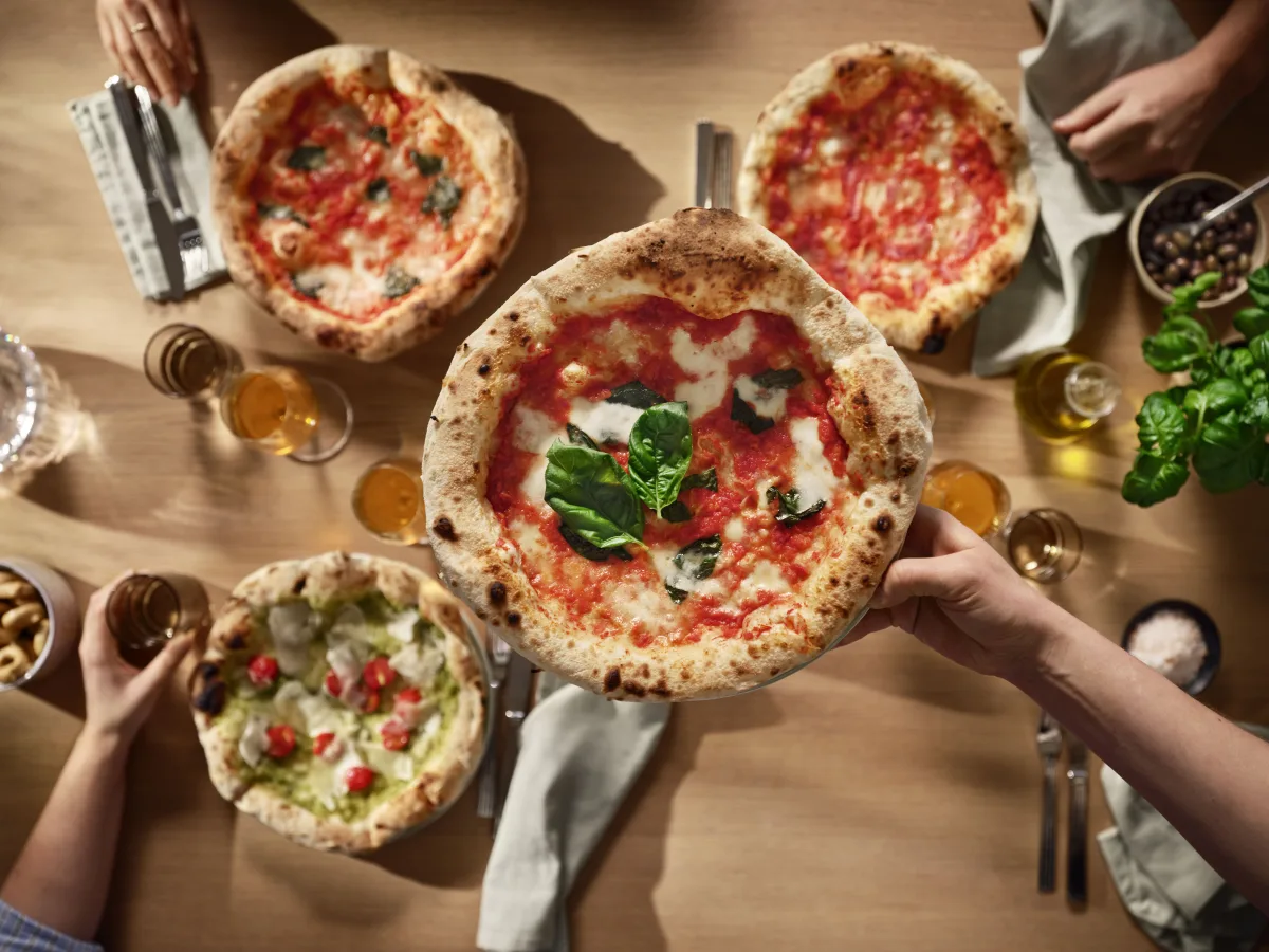 Tavola vista dall'alto con diverse pizze appena sfornate, basilico e olio